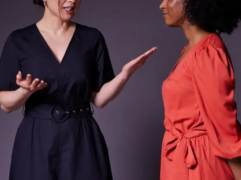Photo of an Asian woman and a black woman facing each other with the Asian woman talking and gesturing