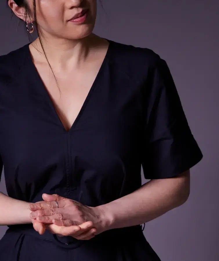 Photo of an Asian woman in a dark dress standing with her hands held together