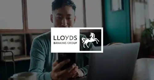 Photo of an Asian man holding a mobile phone in front of his with a white version of the Lloyds Banking Group logo superimposed in the middle foreground