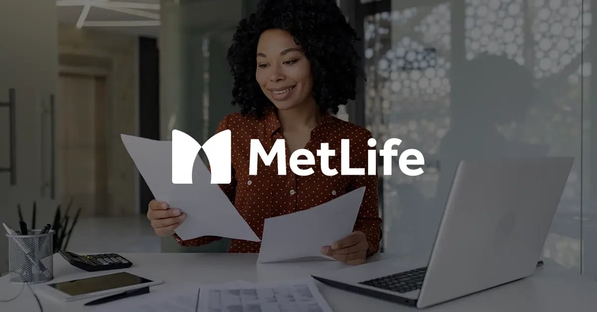 Photo of a woman of colour sat at a desk, smiling and looking a two sheets of paper she's holding with a white version of the MetLife logo superimposed in the middle foreground