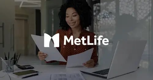 Photo of a woman of colour sat at a desk, smiling and looking a two sheets of paper she's holding with a white version of the MetLife logo superimposed in the middle foreground