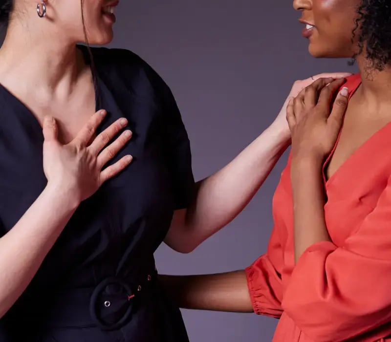 Two women facing each other with one woman placing her hand on the other's shoulder