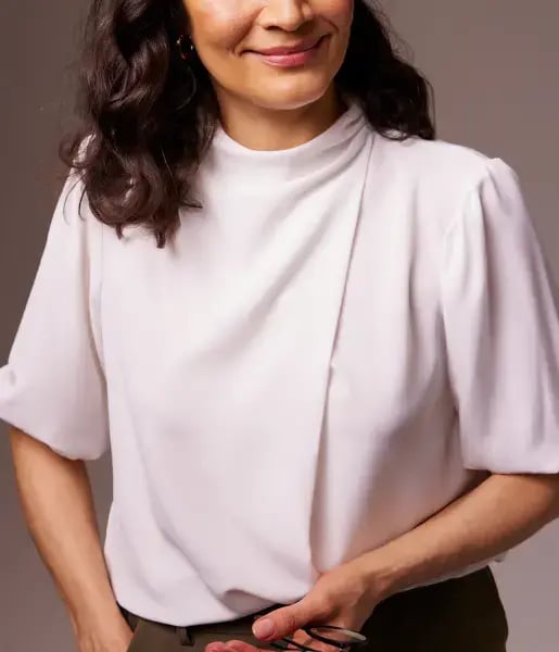 A photo of a woman wearing a white top, holding a pair of glasses and smiling